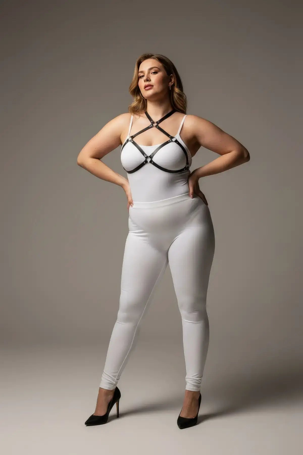 Plus-size black O-ring faux leather chest harness by HarnessClub worn over a white bodysuit