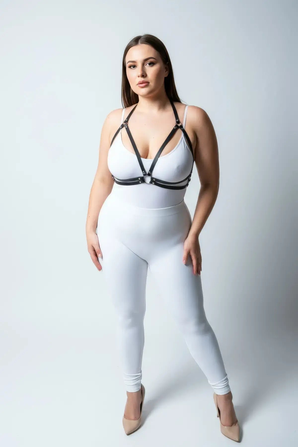 Plus-size black faux-leather O-ring harness worn over a white bodysuit by HarnessClub