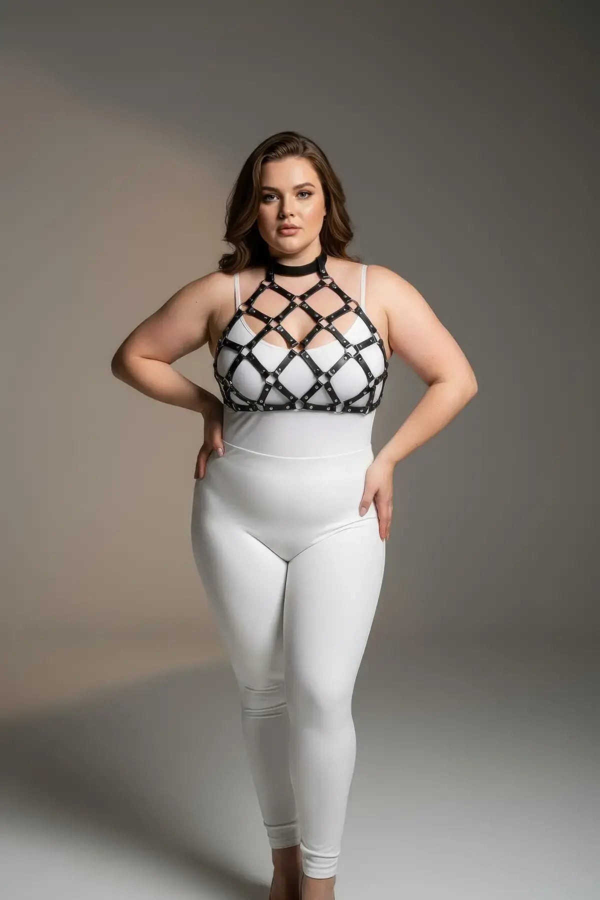 Plus-size black faux-leather O-ring chest harness with lattice straps worn over white bodysuit.