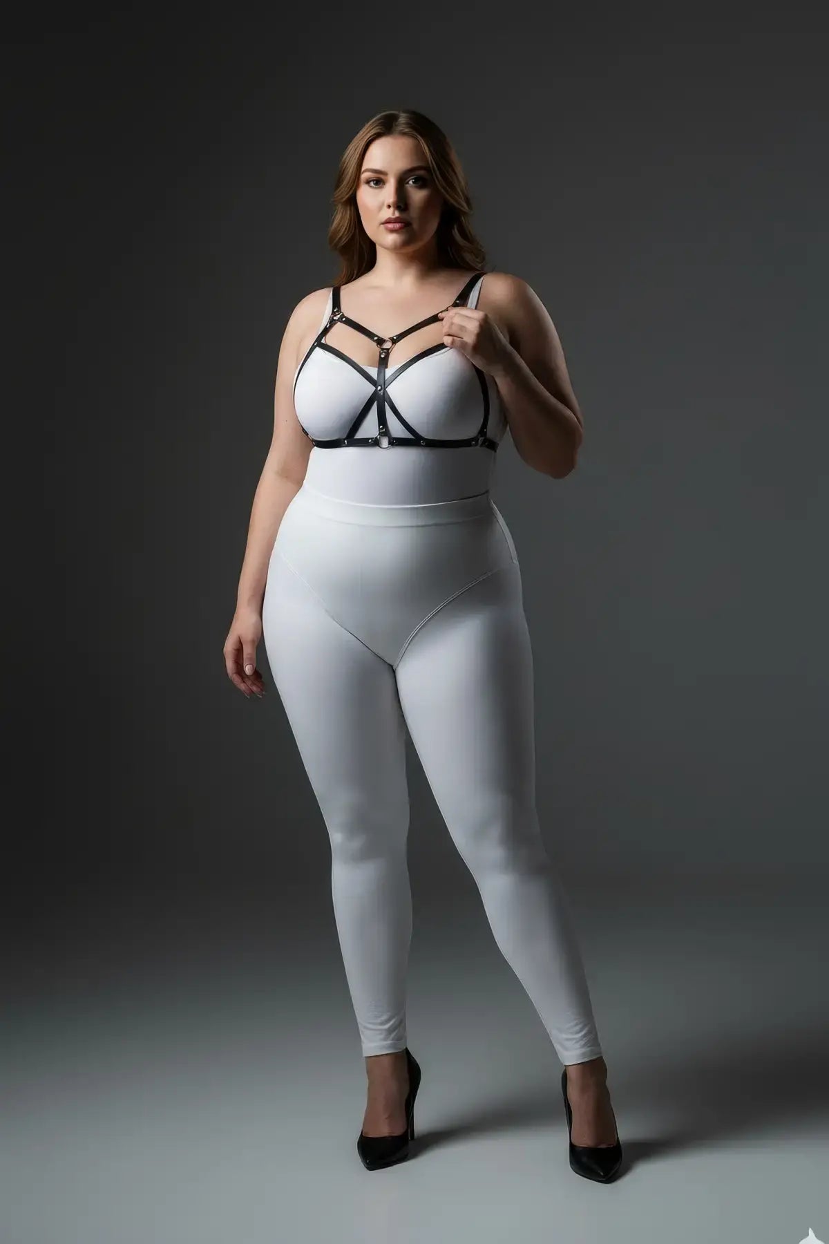 Plus-size black faux leather harness set with O-rings worn over white bodysuit.