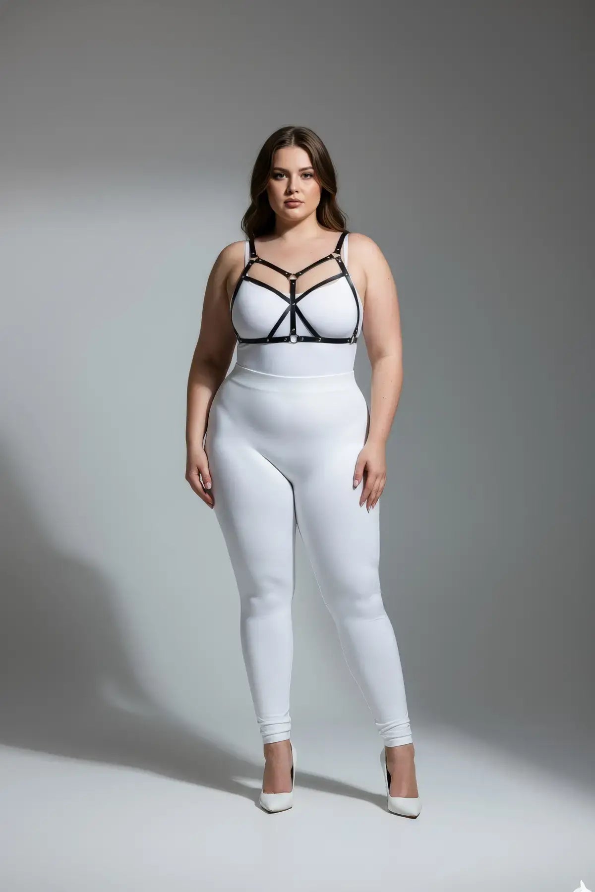 Plus-size black O-ring faux leather harness by HarnessClub on model wearing white bodysuit.