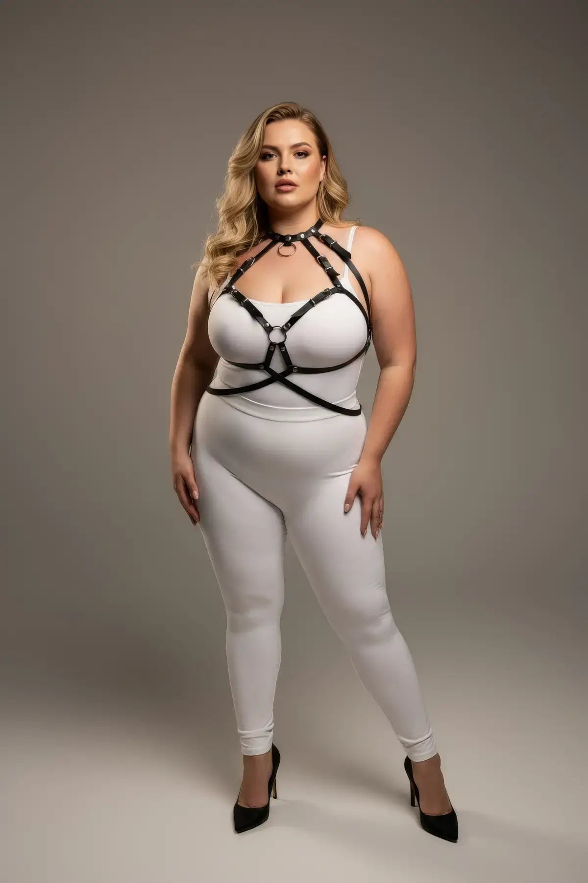 Plus-size black faux-leather O-ring harness over white bodysuit, HarnessClub body accessory.
