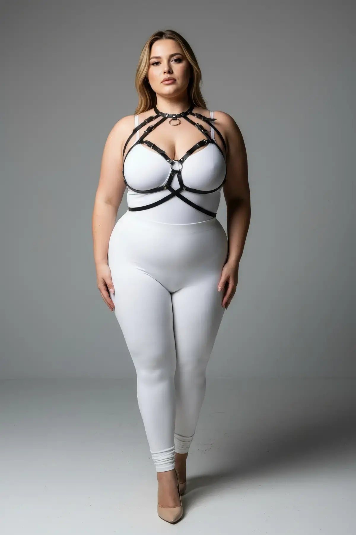 Plus-size black faux-leather O-ring over-outfit harness worn over a white bodysuit