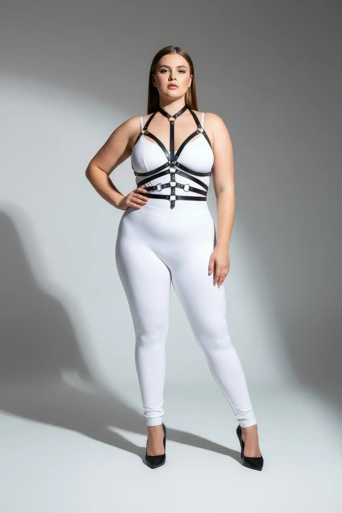 Plus-size black o-ring full-body harness in faux leather worn over a white bodysuit
