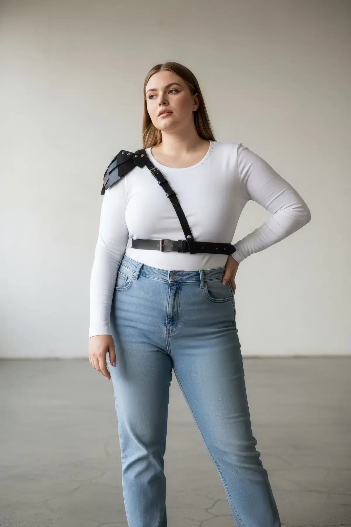 Plus-size black leather shoulder-harness body accessory by HarnessClub, worn over a white top with jeans.