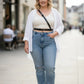 Plus-size black strappy leather belt worn crossbody over a white top and blue jeans