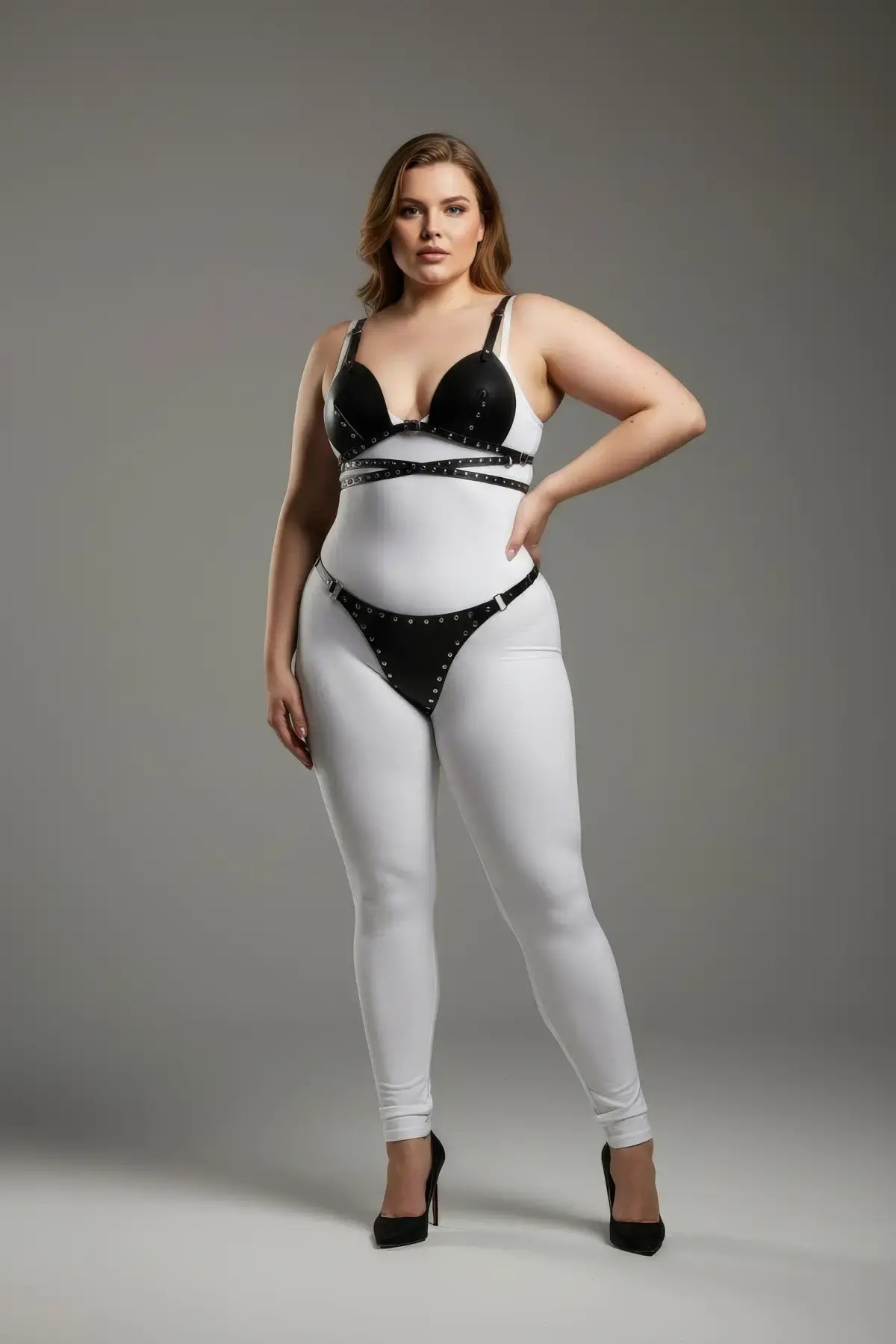 HarnessClub plus-size black stud-detail faux leather harness set worn over a white bodysuit