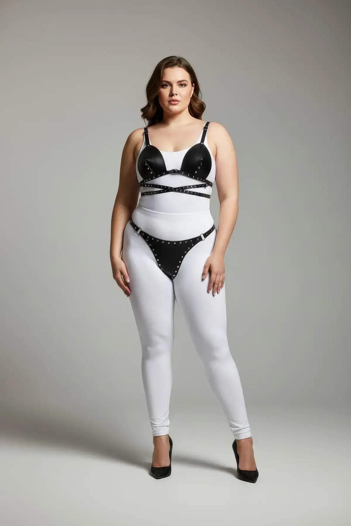 Plus size black stud-detail faux leather harness set by HarnessClub worn over white bodysuit