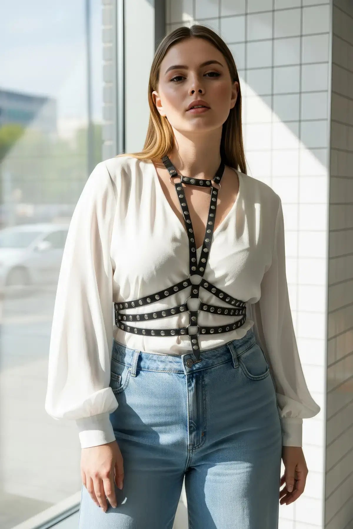Plus size black studded cage harness in vegan leather worn over a white blouse.
