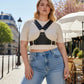Plus Size Black Studded Leather Body Sash by HarnessClub worn over a cream knit top in an outdoor urban street setting.