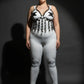 Plus-size black vegan-leather chest harness with studded V-frame and O-ring fringe on white bodysuit.