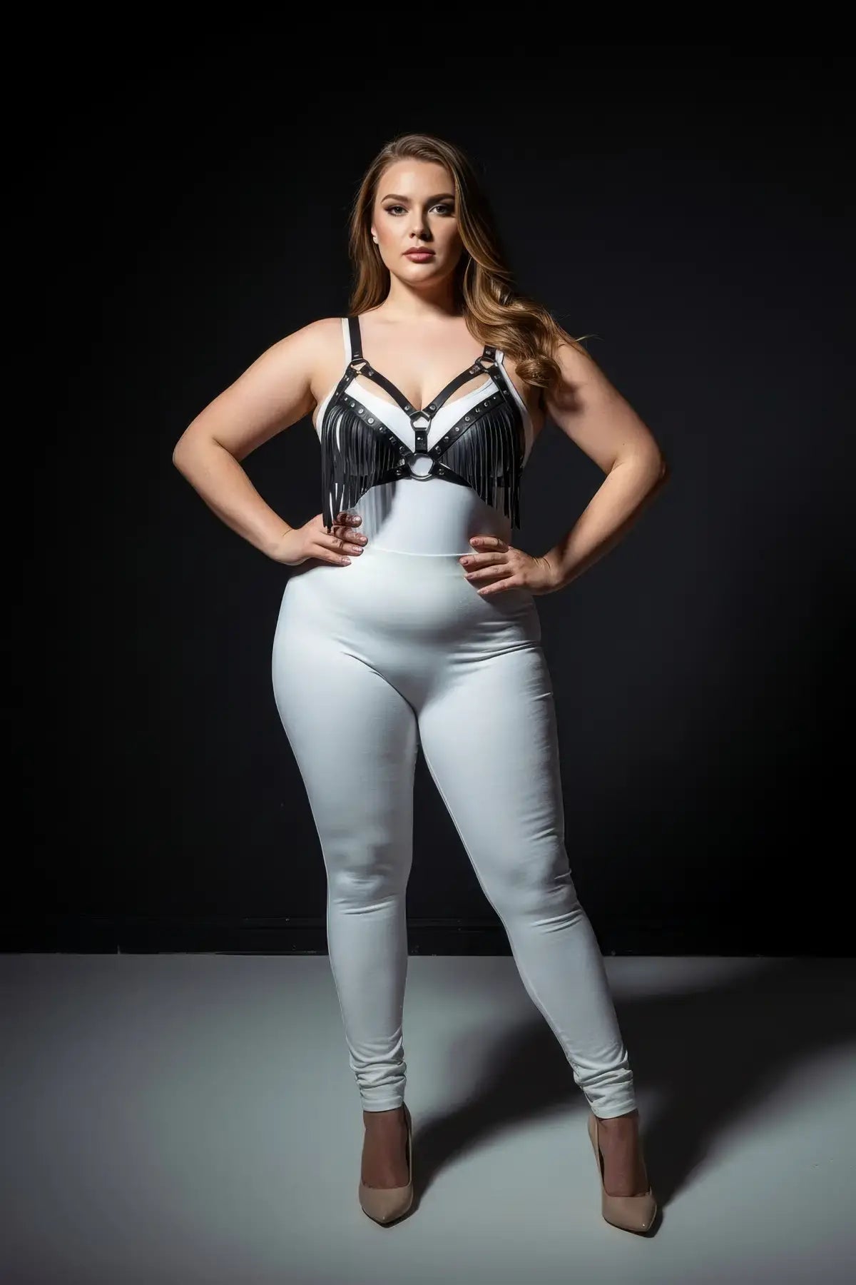 Plus size black tassel-detail faux leather bra harness with fringe, worn over a white bodysuit.