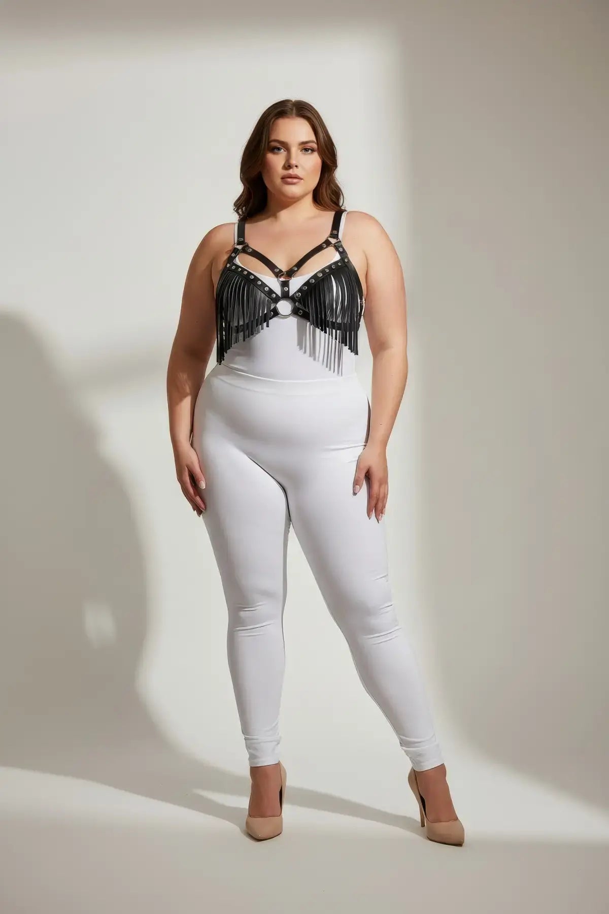 Plus-size black faux-leather tassel bra harness on model with white bodysuit; fringe detailing across the chest.