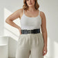 Plus-size black thick double-buckle studded belt worn at waist over white tank top and beige pants.