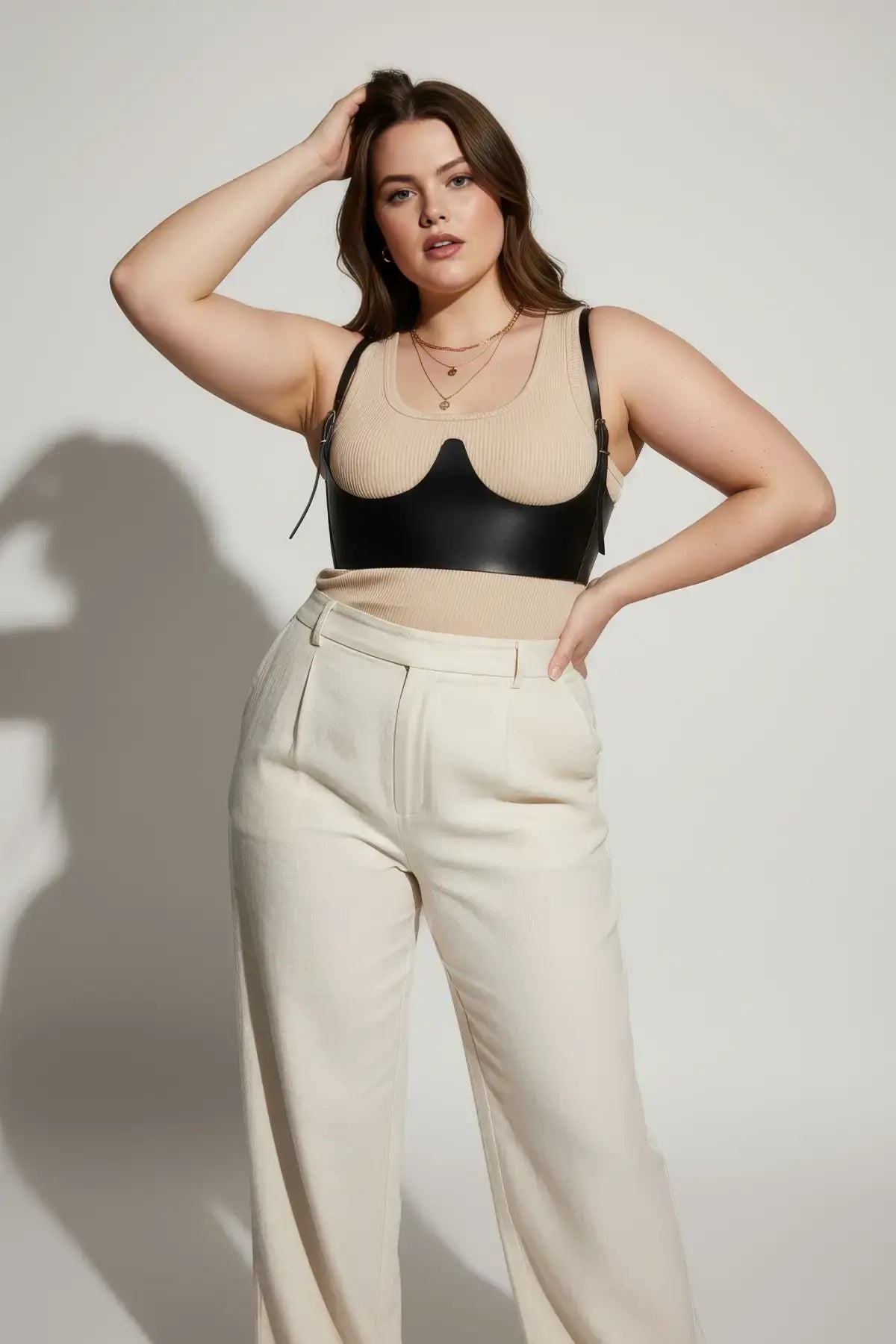 Plus-size black underbust corset with vegan leather shoulder straps, worn over a beige top