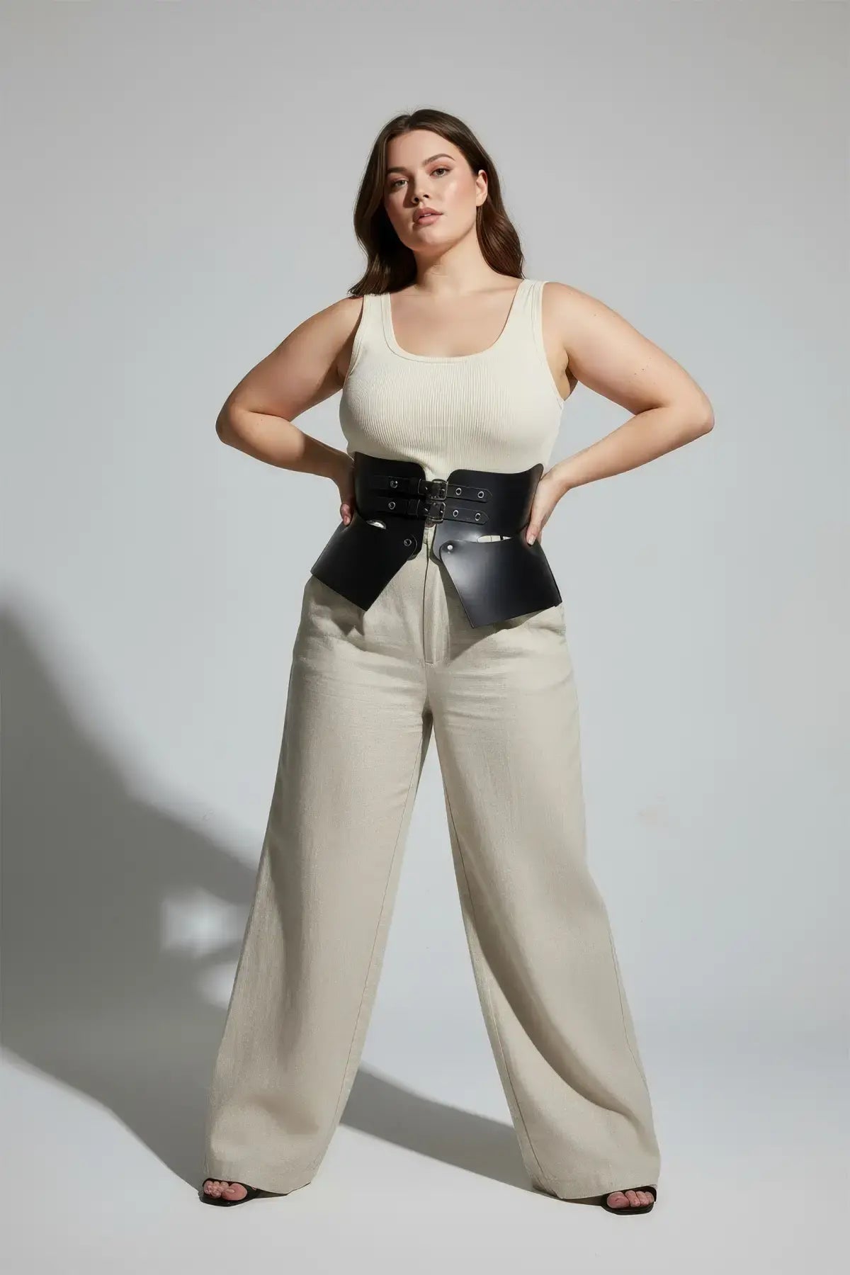 Plus size black vegan-leather wide corset belt with peplum panels worn over cream top and beige pants