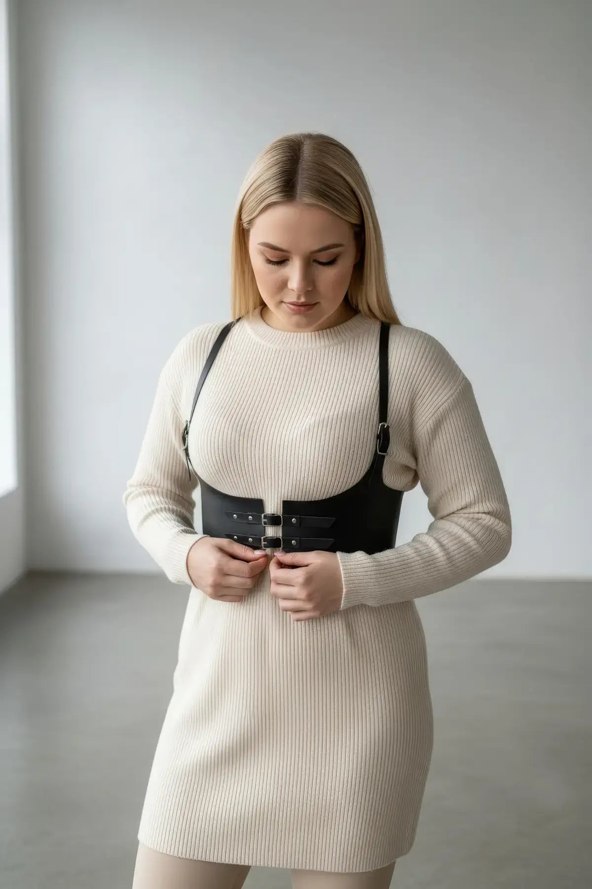 Plus-size black vegan leather under-bust corset harness by HarnessClub, worn over a beige ribbed knit dress