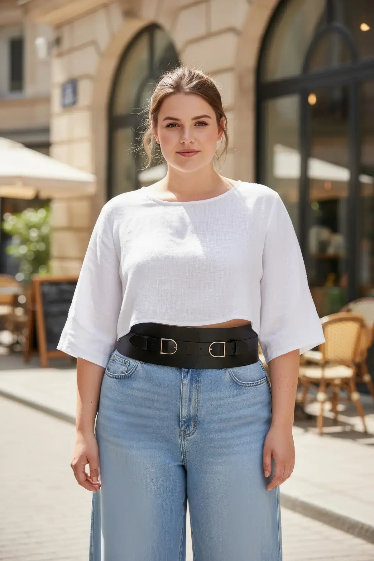 Plus size black wide double-buckle corset belt shown worn over a white top with jeans on a city street