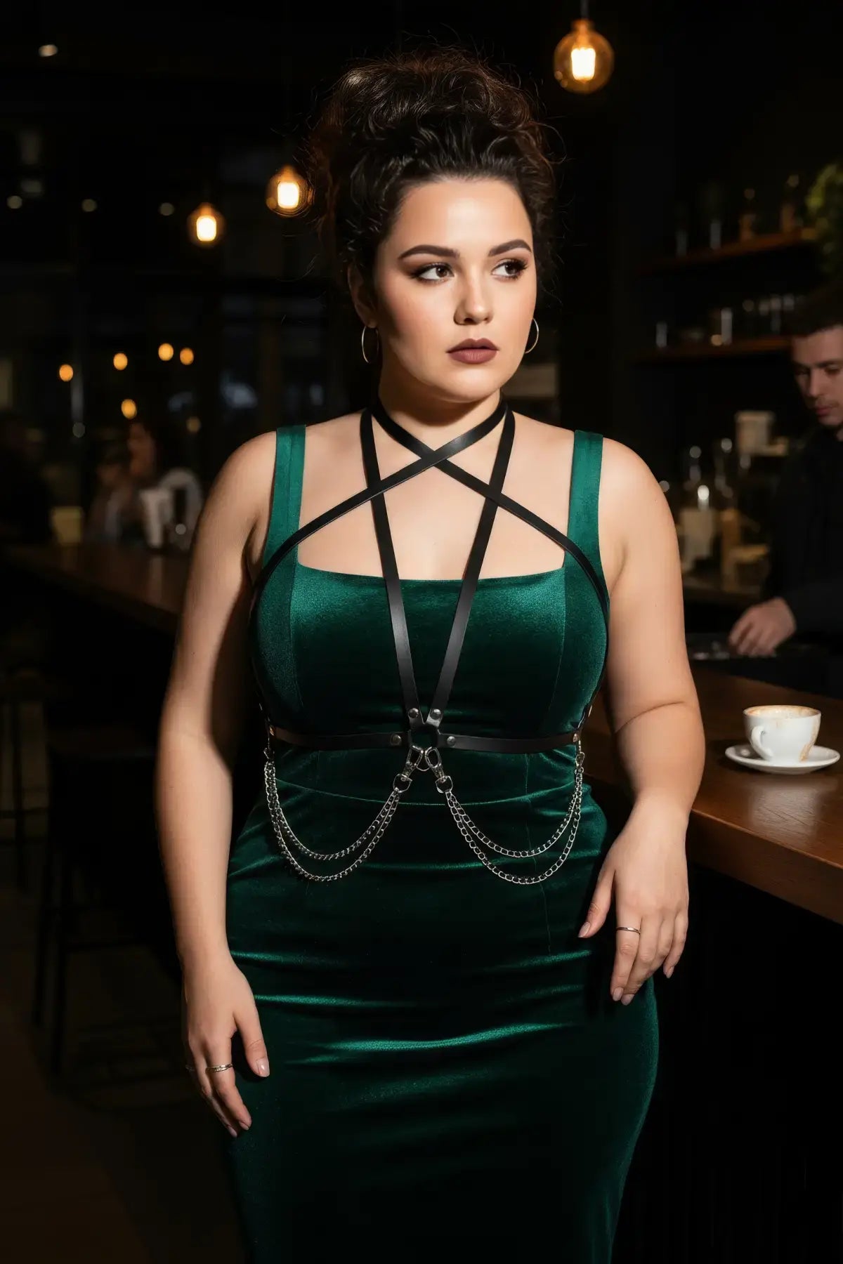 Plus-size black vegan leather X-cross chest harness with chain drops worn over a green velvet dress