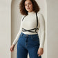 Plus-size black vegan leather X-cross shoulder harness worn over a white turtleneck