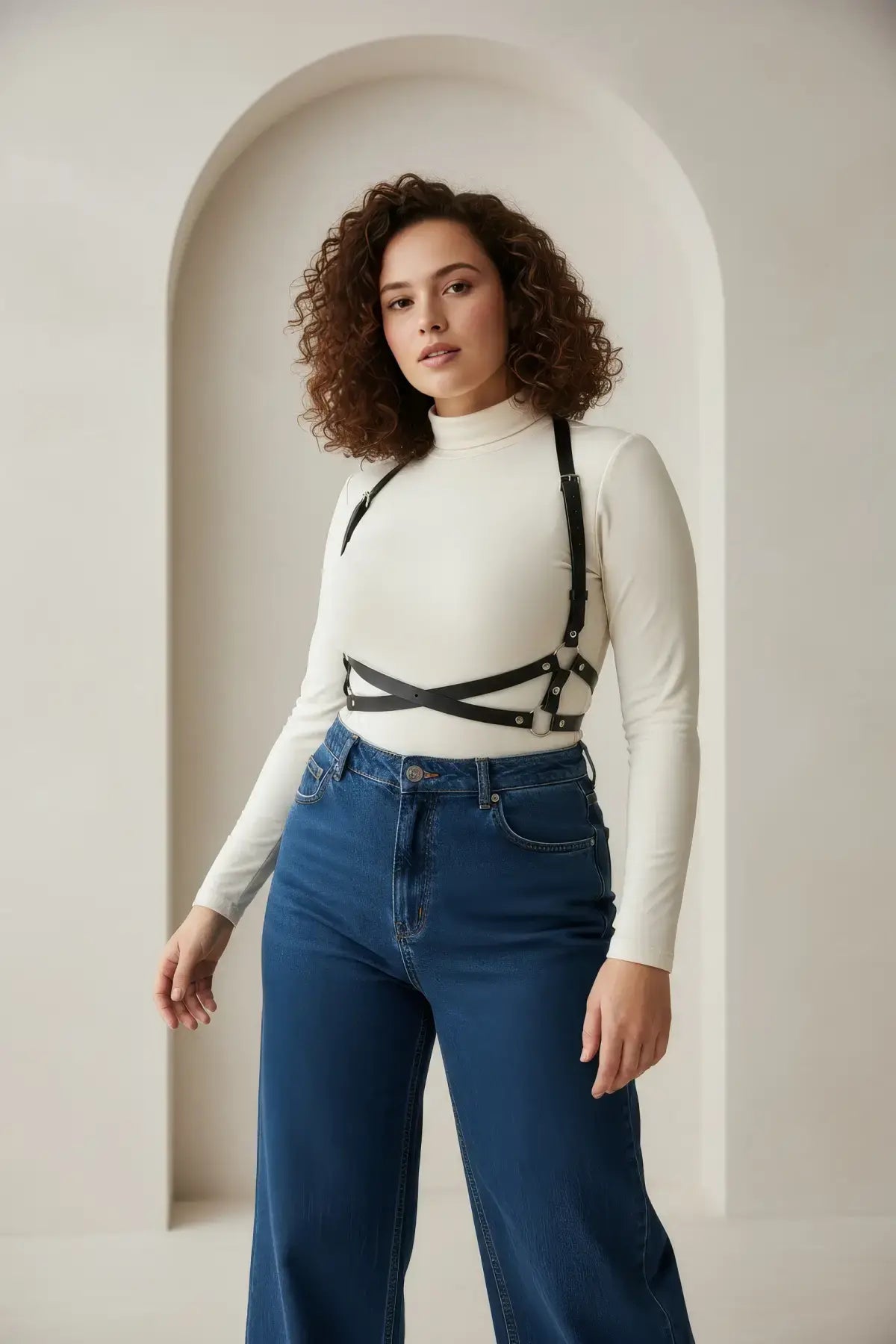 Plus-size black vegan leather X-cross shoulder harness worn over a white turtleneck