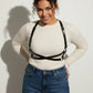 Plus size black X-cross shoulder harness; vegan leather body accessory worn over white knit top.