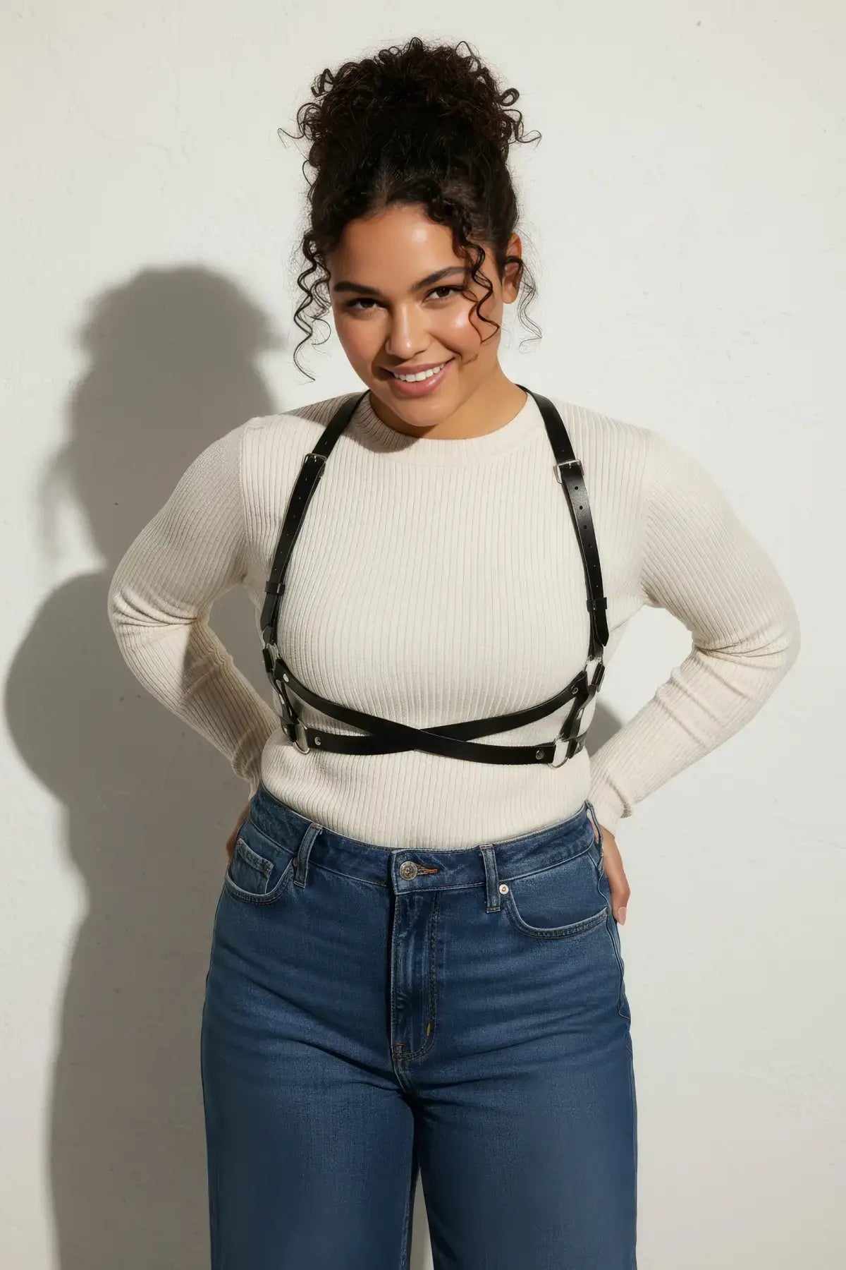 Plus size black X-cross shoulder harness; vegan leather body accessory worn over white knit top.