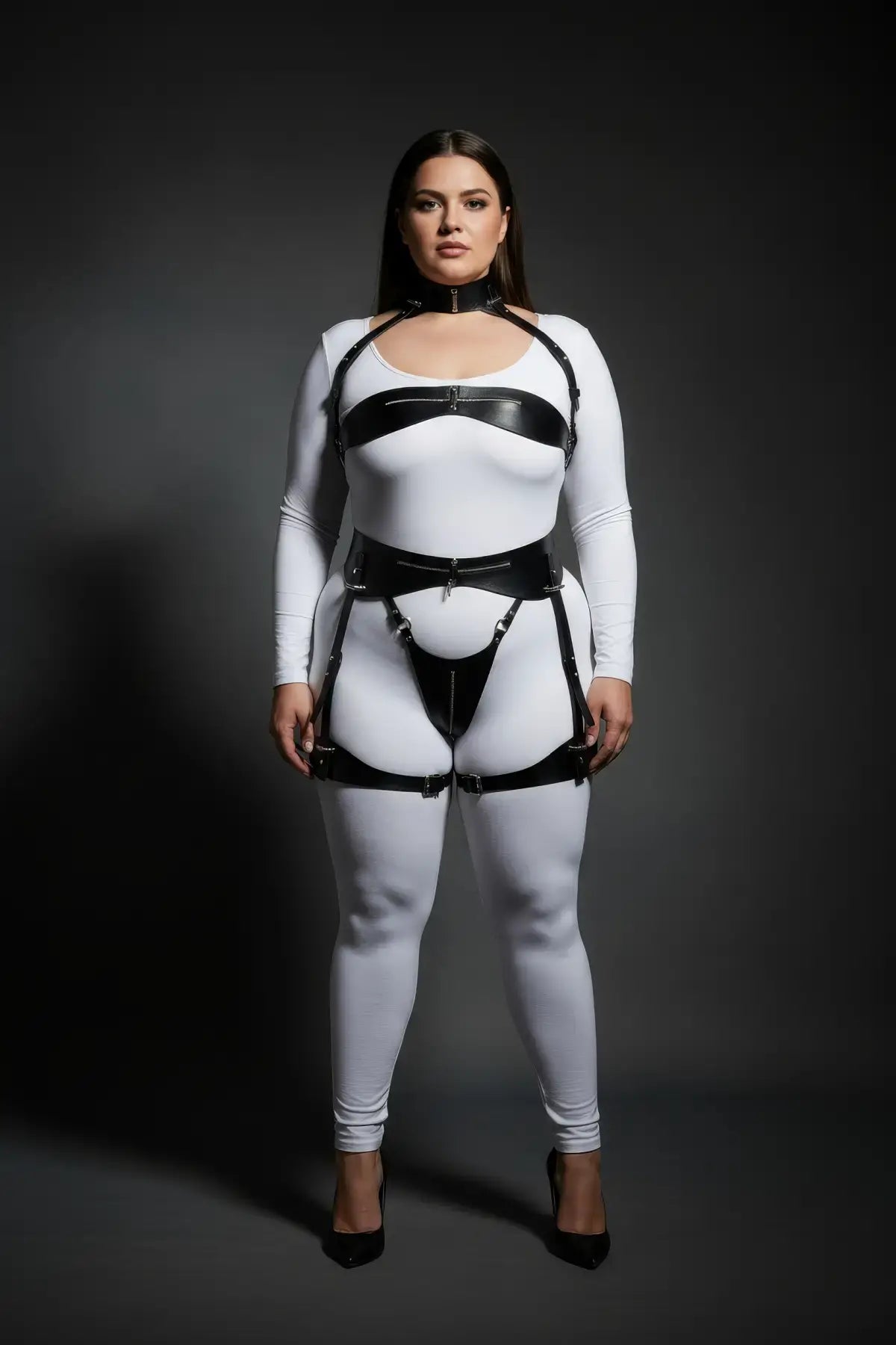 Plus-size black vegan leather harness set with zip-detail chest strap, waist belt and thigh garters on white bodysuit
