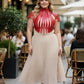 Plus Size Bold Leather Strap Body Harness by HarnessClub, red leather, strappy design worn over beige pleated skirt.
