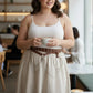 Plus size brown grommet belt with o-ring chain cluster worn over a white ribbed tank top; vegan leather.