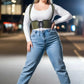 Plus-size khaki corset harness with shoulder straps and lace-up front, worn over a white top with blue jeans.