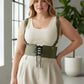 Plus-size khaki corset harness with shoulder straps and lace-up front worn over a cream tank top.