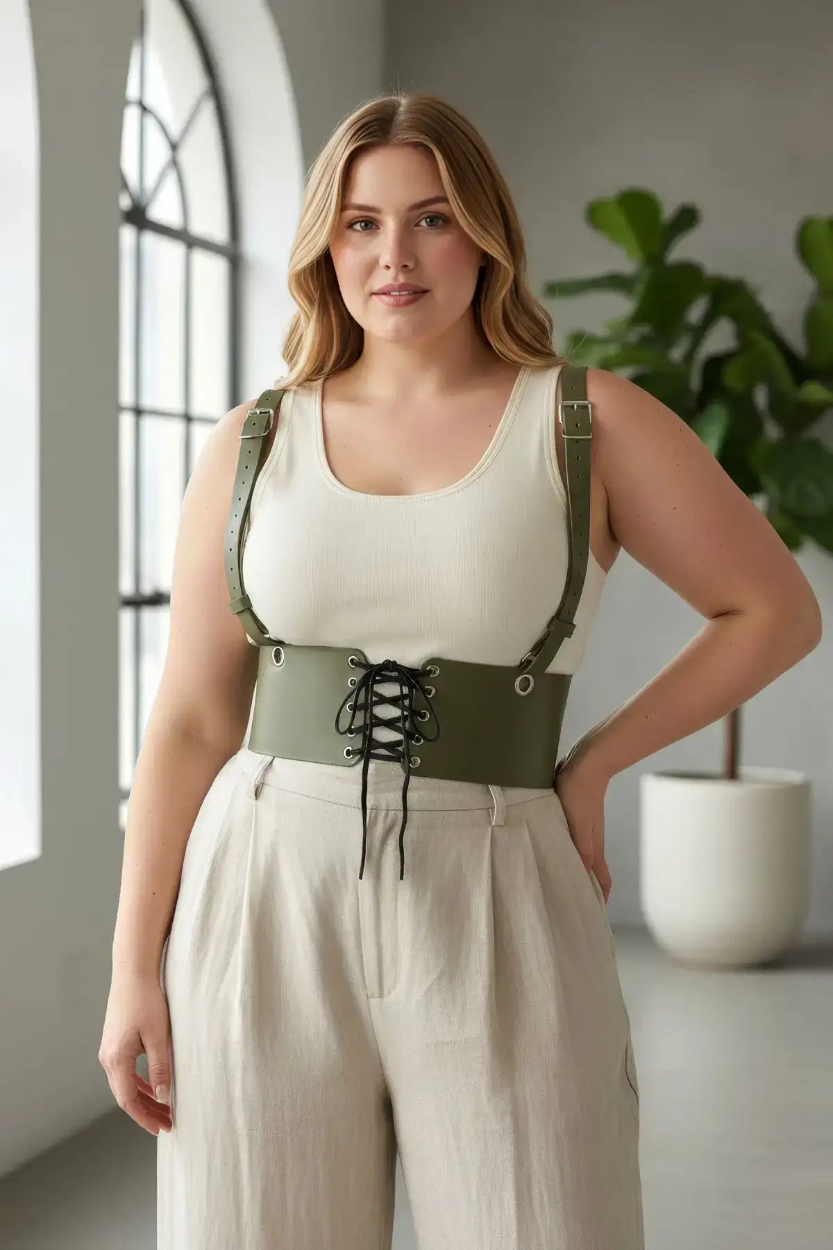 Plus-size khaki corset harness with shoulder straps and lace-up front worn over a cream tank top.