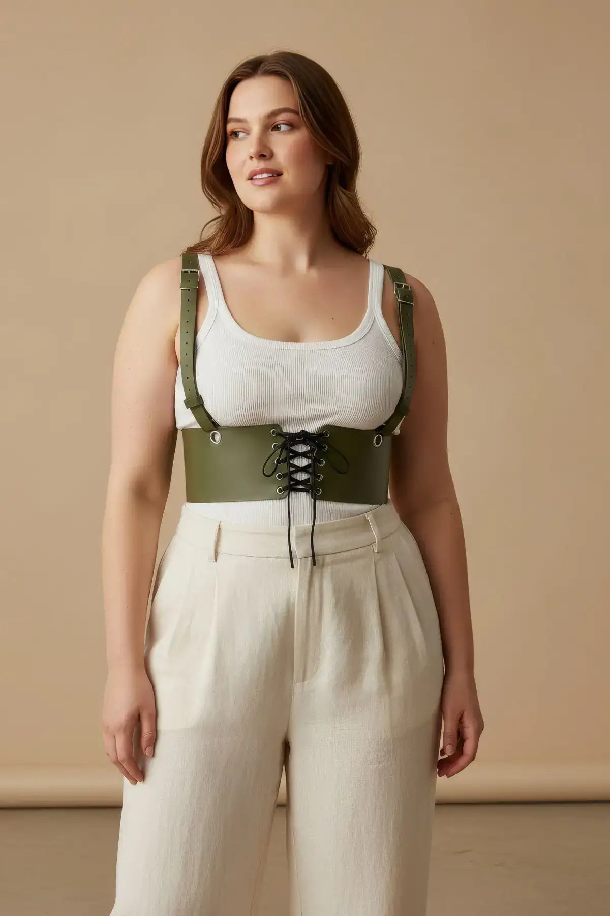 Plus-size khaki corset harness with shoulder straps and lace-up front, worn over a white ribbed tank top.