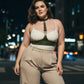 Plus-size khaki leather corset-look body harness worn over a cream top with beige trousers