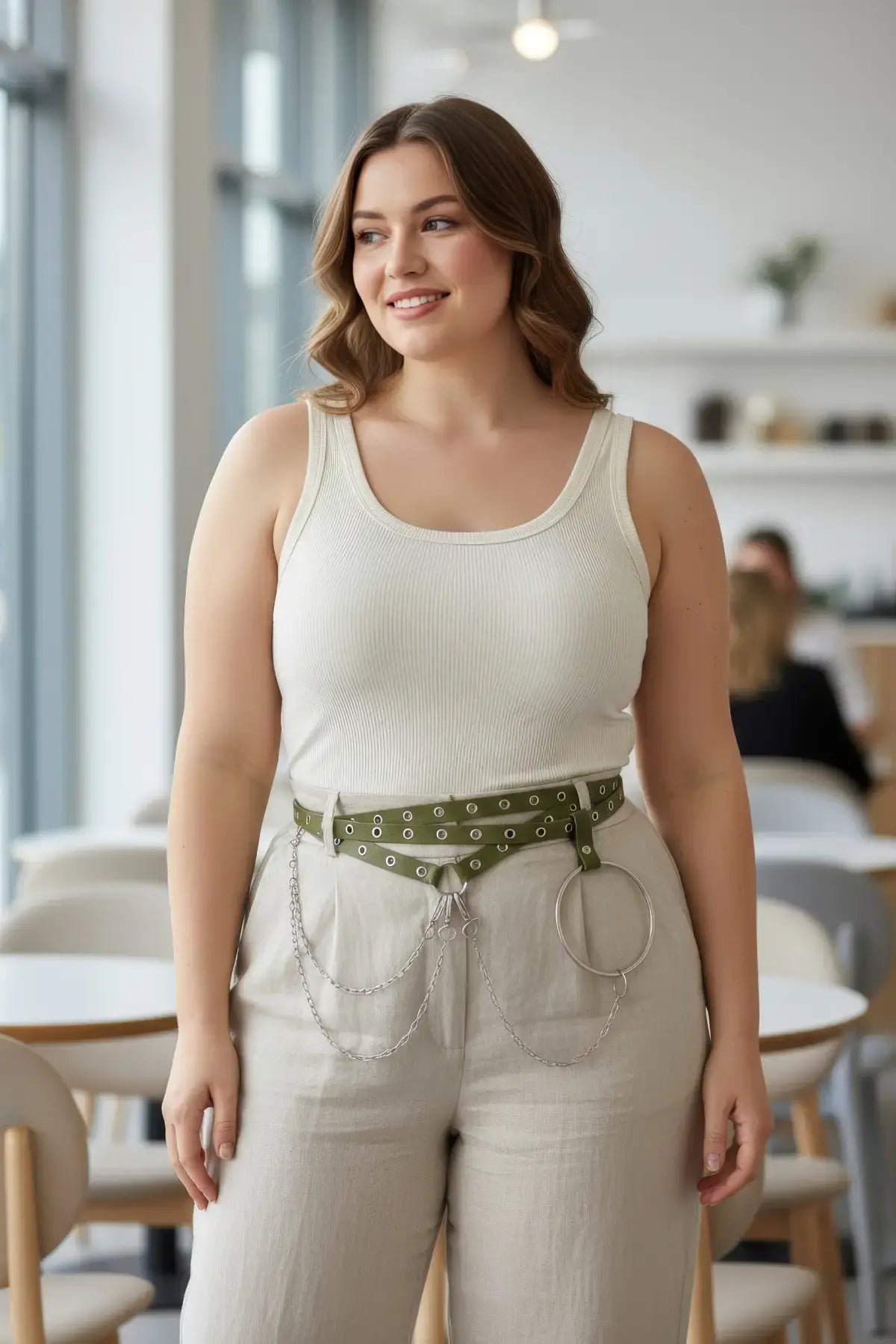 Plus-size khaki double-strap eyelet belt with vegan leather, chains and O-ring worn at the waist over beige pants.