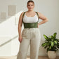 Plus-size khaki lace-up corset belt worn over a white top and beige wide-leg pants.