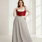 Plus-size red vegan leather lace-up corset harness worn over a cream knit top with a gray pleated maxi skirt