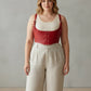 HarnessClub plus-size red vegan-leather lace-up corset harness worn over a beige top.