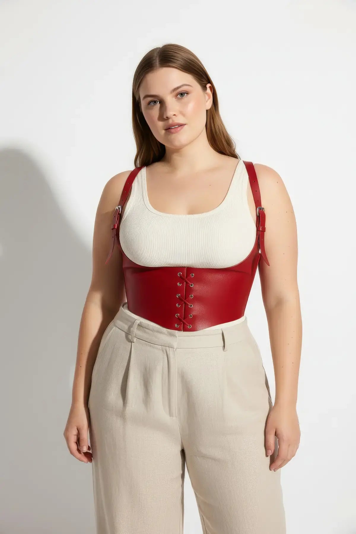 Plus-size red vegan-leather lace-up corset harness worn over a white tank top.