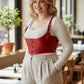Plus Size red vegan leather lace-up corset harness worn over a beige top in a cafe.