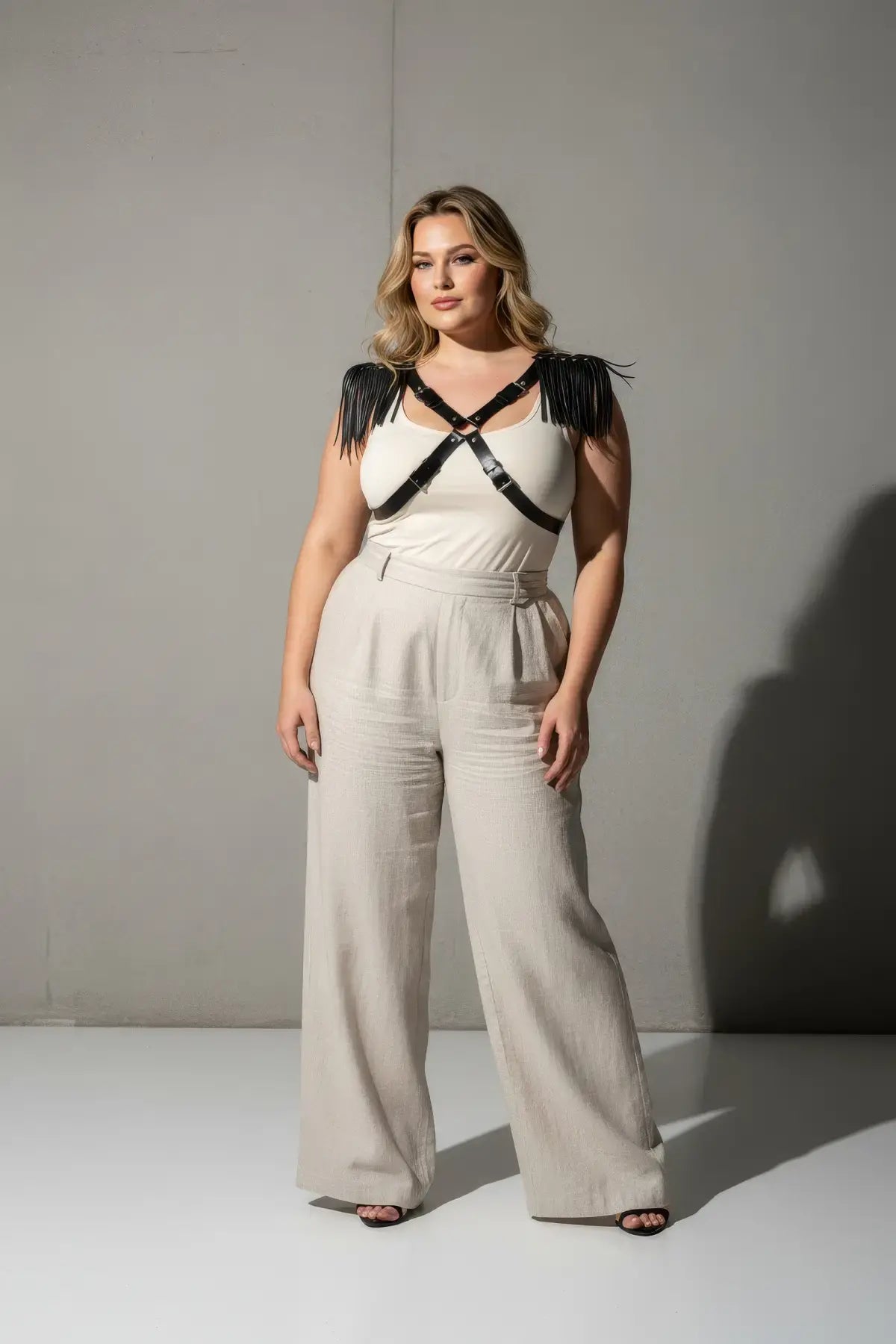 Plus-size leather body harness with shoulder tassels, black cross-strap design worn over a white top.