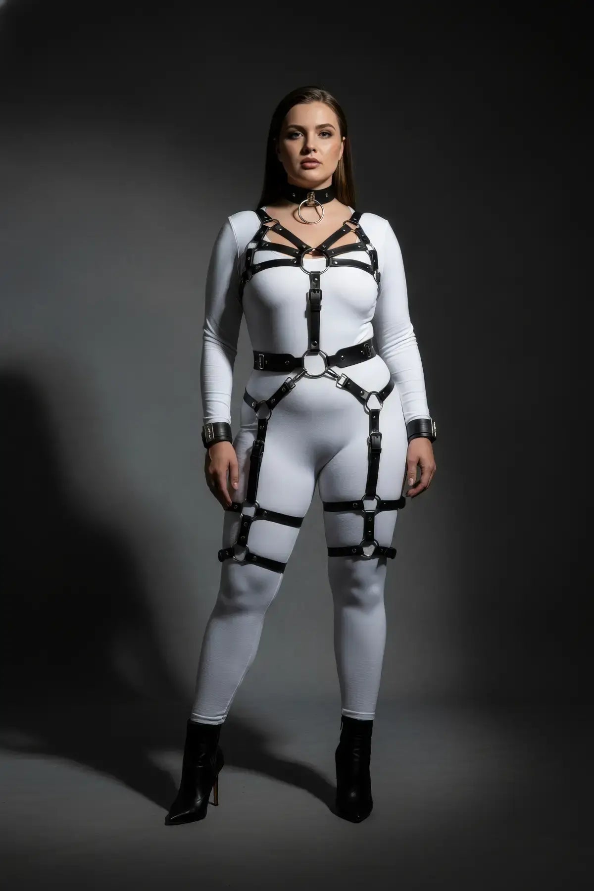 Plus-size multi-strap body harness set with wrist cuffs and garter in vegan leather, by HarnessClub, worn over a white bodysuit.