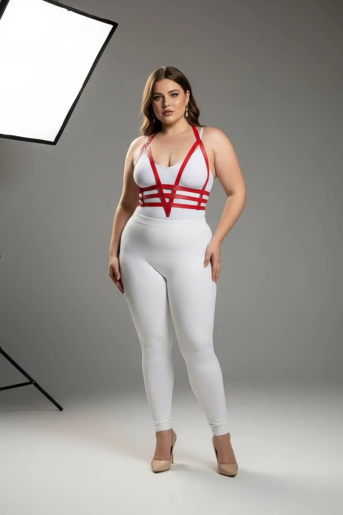 Plus size red adjustable faux leather body harness by HarnessClub worn over a white bodysuit.