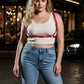 Plus-size red adjustable strappy leather body belt worn over a white ribbed tank top by HarnessClub.