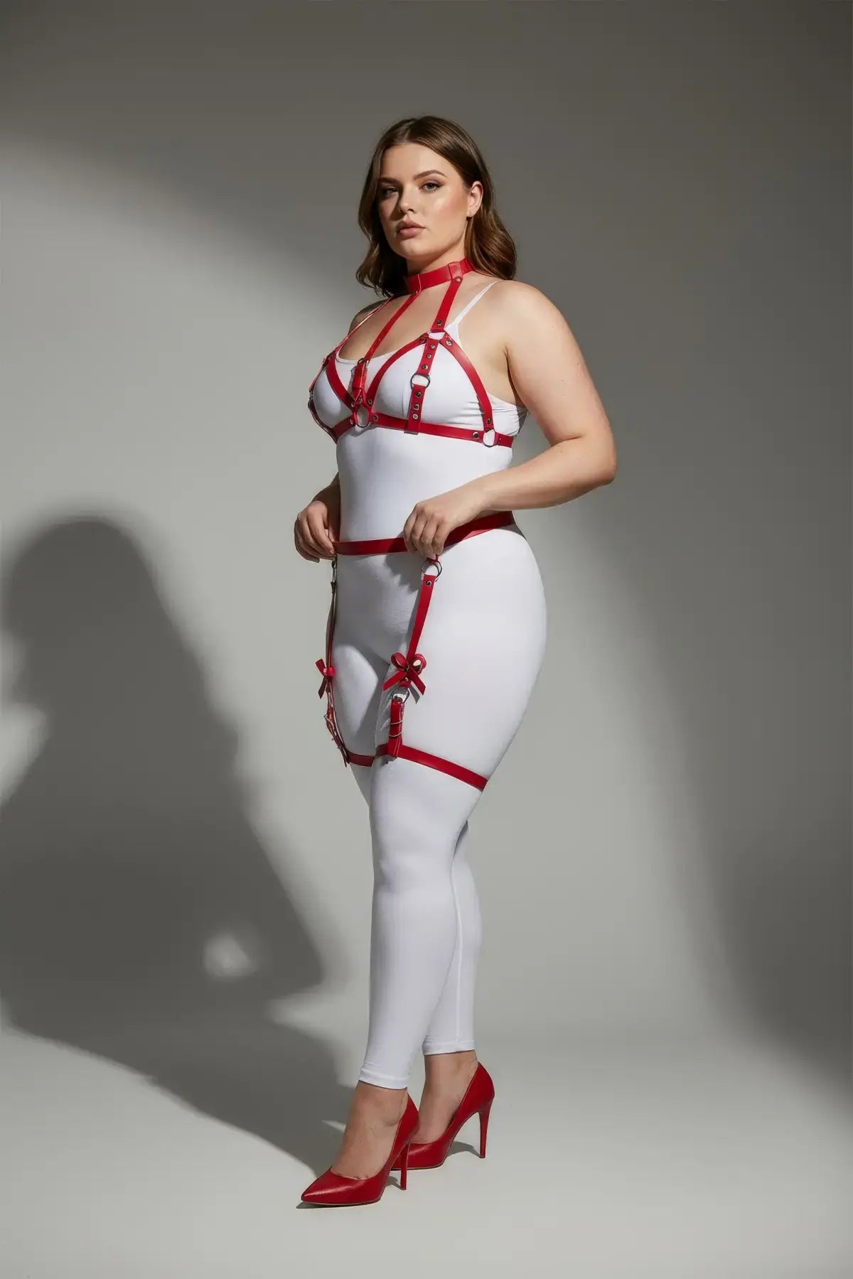 Plus-size red bow-detail faux leather garter harness set worn over a white bodysuit by HarnessClub