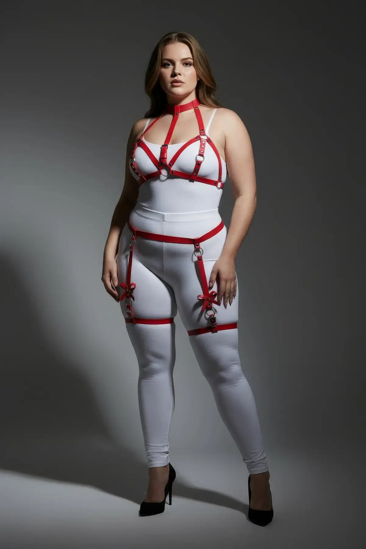 Plus-size red bow-detail faux leather garter harness worn over white bodysuit; model in black heels.