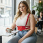 Plus-size red studded leather corset-style accessory by HarnessClub worn over a white tank