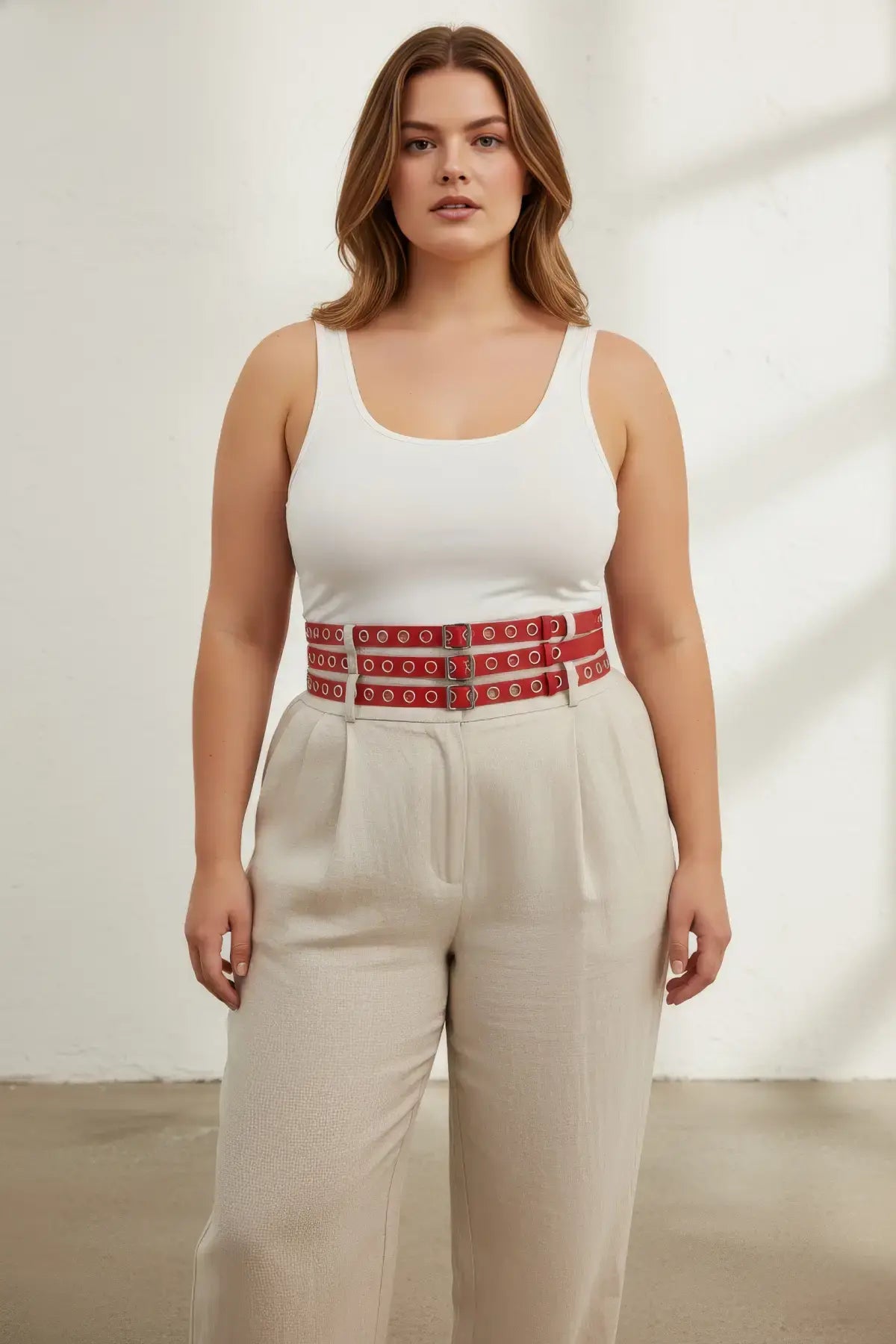 HarnessClub plus-size red double-row grommet belt with multiple buckles, vegan leather, worn at waist over a white top.