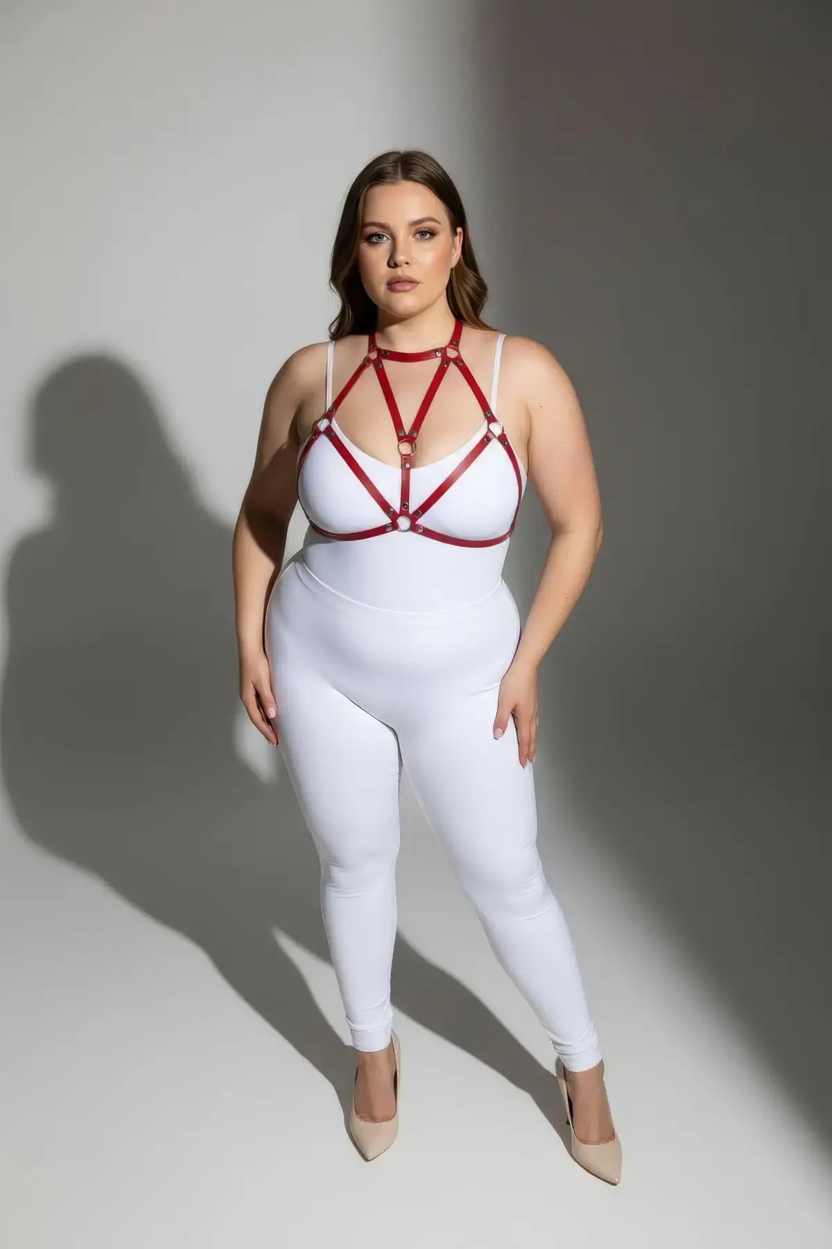 Plus-size red faux-leather O-ring body harness worn over a white bodysuit.